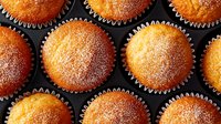 Freshly baked vanilla cupcakes dusted with powdered sugar arranged in baking tin, top view close up. Golden brown muffins with crispy tops create appetizing pattern.