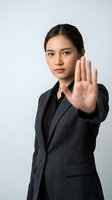Professional Asian businesswoman in dark suit making stop gesture with hand raised against white background for corporate communication concepts.