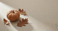 Autumn pumpkin with fallen maple leaves on neutral beige surface creating warm seasonal atmosphere for fall decorating and harvest celebrations.