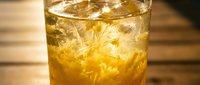 Chilled whiskey cocktail in a rocks glass with ice cubes on a wooden bar surface, golden amber drink glowing in warm light.