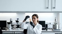 Female scientist examining sample in modern laboratory with microscopes and equipment for research analysis.