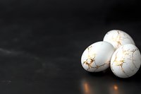 White cracked eggs with golden veins on dark background, dramatic lighting creates mysterious atmosphere. Luxury food styling concept for design projects.