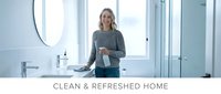 Young blonde woman cleaning modern bathroom with spray bottle and cloth in bright contemporary home interior with large windows and minimalist design.