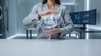 Professional businesswoman in gray suit protecting holographic trust symbol with hands in modern office environment showcasing corporate security concepts.