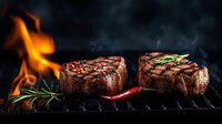 Juicy grilled beef tenderloin steaks with rosemary and chili pepper on black grill grate with flames and smoke in dark background. Cooking premium meat.