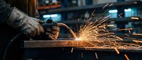 Industrial worker using angle grinder on metal surface creating bright sparks in manufacturing workshop environment for metalworking projects.