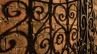 Ornate wrought iron gate with decorative scrollwork casting intricate shadows on textured stone wall surface in warm golden light for architectural design.
