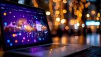 Laptop computer displaying colorful bokeh lights on screen with warm golden holiday lights creating magical atmosphere in background for digital creativity.