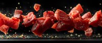 Fresh raw beef cubes falling on dark background with spices and herbs, dramatic food photography with motion effect and splash of seasoning.