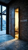 Open rustic metal door in industrial brick loft with welcome sign, warm glowing room interior, city skyline view, urban architecture concept.