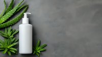 White cosmetic pump bottle with fresh aloe vera leaves on gray concrete background for natural skincare and beauty product mockup design.