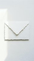 White handmade paper envelope with deckled edges on light background, soft shadows, elegant stationery for wedding invitations and correspondence.