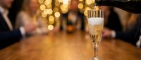 Champagne being poured into a flute glass at an elegant celebration or party with bokeh lights and guests in the background.
