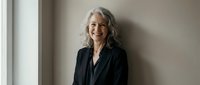 Confident mature Caucasian businesswoman with gray hair smiling in modern office interior wearing professional black blazer for corporate lifestyle.