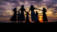 Group of women silhouettes holding hands in circle dance against dramatic sunset sky. Sisterhood, unity, friendship and celebration concept.