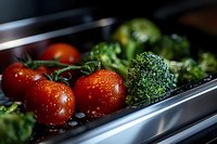 Fresh red tomatoes on vine and green broccoli florets with water droplets in metal cooking tray, macro food photography with selective focus.