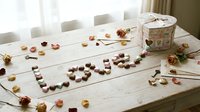 Chocolates arranged in the word love on a rustic wooden table with dried roses, petals, vintage keys, and a floral gift box for Valentine's Day.