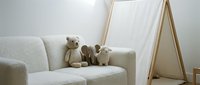 Cozy nursery interior with teddy bears on gray armchair and wooden teepee tent creating warm child bedroom atmosphere for family home decor.