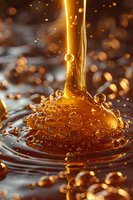 Flowing golden honey stream creating bubbles and ripples against dark background, captured in macro with bokeh effect and dramatic lighting for food packaging.