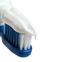 Blue toothbrush with white toothpaste on bristles isolated on white background for dental hygiene and oral care design projects.