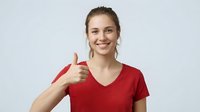 Happy young Caucasian woman in red v-neck t-shirt showing thumbs up gesture with bright smile on white background for positive marketing campaigns.