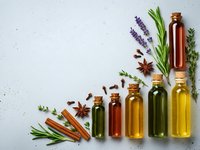 Natural essential oil bottles with fresh herbs and spices arranged on white background for aromatherapy and wellness products.