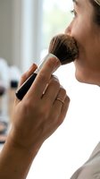 Woman applying powder blush with brush to cheek, close-up beauty and cosmetics makeup routine for skincare and facial enhancement.
