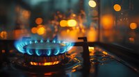 Blue flame of gas stove burner against dark background with golden bokeh lights, close up view showing energy consumption and cooking concept.