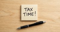 Yellow sticky note with TAX TIME handwritten message and black pen on wooden desk surface for accounting and financial planning reminders.