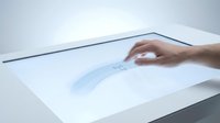 Male hand touching interactive touchscreen display with blue digital wave interface on white surface.