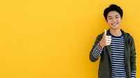 Young Asian male teenager wearing olive green jacket and striped shirt giving thumbs up gesture against bright yellow background, expressing approval and positivity for advertising and promotional campaigns.