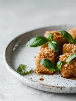 Crispy phyllo pastry rolls garnished with fresh basil leaves served on rustic ceramic plate against light background, selective focus food photography.