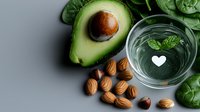 Fresh halved avocado with almonds and glass of water garnished with mint leaves on gray background, healthy fats and clean eating concept for wellness.