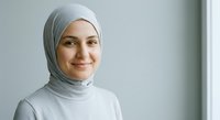 Young Muslim woman in gray hijab and white top smiling warmly at camera in bright modern interior space for lifestyle and diversity concepts.