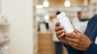 Man holding white medicine bottle in pharmacy or healthcare setting for pharmaceutical product mockup and medical advertising.