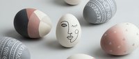 Modern Easter eggs with abstract face art and geometric patterns in pastel pink, gray, and white colors on neutral background for spring decoration.