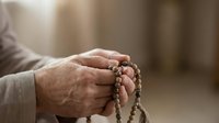 Elderly man hands holding prayer beads during meditation and spiritual practice in peaceful indoor setting for mindfulness and religious devotion.