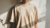 Young Asian person wearing beige oversized t-shirt standing in natural window light with dramatic shadows creating minimalist aesthetic composition.