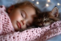 Young girl and gray tabby cat sleeping peacefully together under soft pink knitted blanket with bokeh lights creating dreamy atmosphere in background.
