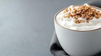 Creamy cappuccino with whipped cream and chocolate shavings in white ceramic cup on gray surface. Hot coffee beverage for cafe menu and morning routine concepts.