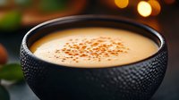 Creamy pumpkin soup served in textured black bowl with nutmeg garnish, soft bokeh background creates cozy autumn atmosphere. Perfect for seasonal menu design.