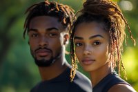 Young African American couple with dreadlocks looking at camera outdoors in natural sunlight with green bokeh background for lifestyle photography.