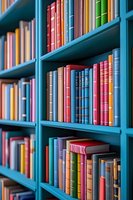 Colorful hardcover books arranged on bright turquoise library shelves creating vibrant pattern of spines in red, blue, green and yellow tones, selective focus background.