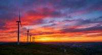 Wind turbines generating renewable energy against dramatic sunset sky with vibrant orange and purple clouds over rolling countryside landscape.