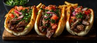 Grilled steak tacos on soft rolls topped with fresh tomatoes, red onions and chopped cilantro served on wooden board against dark background.
