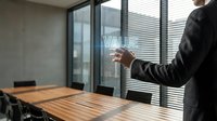 Business professional presenting value proposition on glass wall in modern conference room with wooden table and city view through windows.