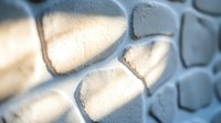 Textured white stone wall with dramatic shadows creating depth and dimension, architectural detail in natural sunlight for modern interior design background.