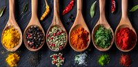 Colorful spices and herbs in wooden spoons on dark background, variety of seasonings including turmeric, paprika, peppercorns and dried herbs for cooking.