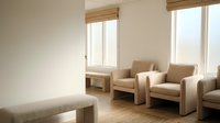 Modern minimalist waiting room with beige armchairs and natural light from large windows creating calm professional atmosphere for healthcare or office space.
