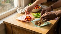 Unrecognizable person preparing fresh vegetables and legumes on wooden counter by window for healthy meal preparation and cooking.